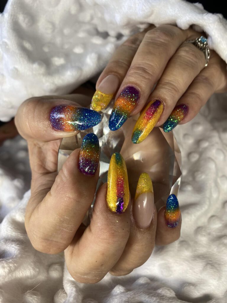 rainbow coloured nailed holding a crystal over a white blanket